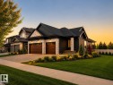 Modern Craftsman-style exterior featuring a dark facade with stone accents, twin wood-panel garage doors, a covered porch with stone columns, and manicured landscaping with integrated lighting - 149 Eastgate Way, St. Albert, AB 