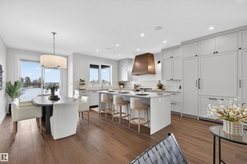 Gourmet kitchen and dining area featuring wide plank wood-finish flooring, white shaker cabinetry, an integrated refrigerator, a large island with counter seating, and a wood-finish range hood - 149 Eastgate Way, St. Albert, AB 