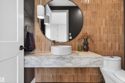 Modern vanity featuring a vessel sink, floating stone countertop, and circular mirror - 