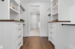 Custom closet system featuring wood-finish flooring, white cabinetry with dark hardware, integrated shelving, and hanging rods - 