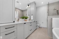 Modern bathroom featuring a dual vanity with light gray cabinetry, white countertops, and black hardware - 