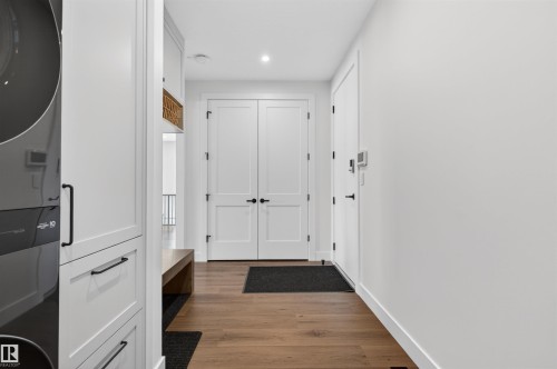 Dedicated laundry area with a stacked appliance unit, custom white cabinetry, and wood-finish flooring - 149 Eastgate Way, St. Albert, AB 