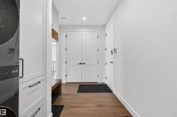 Dedicated laundry area with a stacked appliance unit, custom white cabinetry, and wood-finish flooring - 
