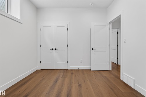 Bright interior space featuring wood-finish flooring, white walls, white trim, white two-panel doors with matte black hardware, and a high horizontal window - 149 Eastgate Way, St. Albert, AB 