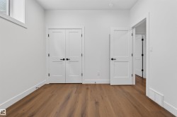 Bright interior space featuring wood-finish flooring, white walls, white trim, white two-panel doors with matte black hardware, and a high horizontal window - 