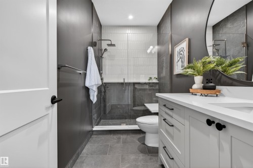 Contemporary bathroom featuring a light gray vanity with a white countertop and dark hardware, a spacious walk-in shower with glass enclosure, a wall-mounted rain shower head, and gray large format tile flooring - 149 Eastgate Way, St. Albert, AB 