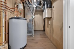 Dedicated utility space featuring a water heater with extensive copper plumbing, forced air furnace, and wood-finish flooring - 