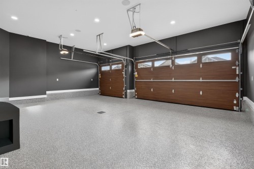 Spacious two-car garage featuring a speckled epoxy floor coating, dark wood-finish garage doors with upper window panels, and recessed ceiling lighting - 149 Eastgate Way, St. Albert, AB 