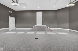 Spacious garage featuring a light gray flake epoxy floor, neutral gray walls, white baseboards, and two white entry doors - 