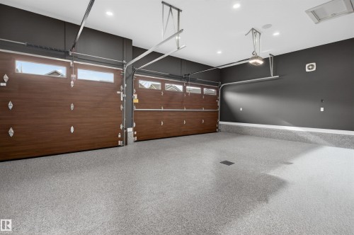 Spacious garage featuring two wood-finish overhead doors with window accents, a durable epoxy coated floor, recessed ceiling lighting, and dark-toned walls - 149 Eastgate Way, St. Albert, AB 