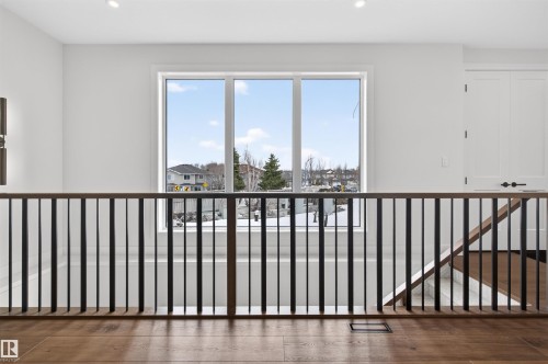 Modern open concept landing featuring a large three-panel window, dark wood-finish flooring, and a sleek black metal and wood-finish railing - 149 Eastgate Way, St. Albert, AB 