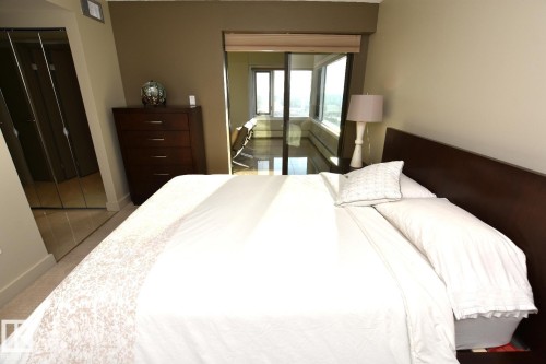 Bedroom featuring a dark wood-finish headboard, beige wall paint, and mirrored closet doors - 1805 10011 123 Street, Edmonton, AB 