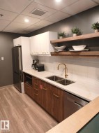 Contemporary kitchen featuring wood-finish lower cabinetry, white upper cabinetry, and a stainless steel refrigerator - 
