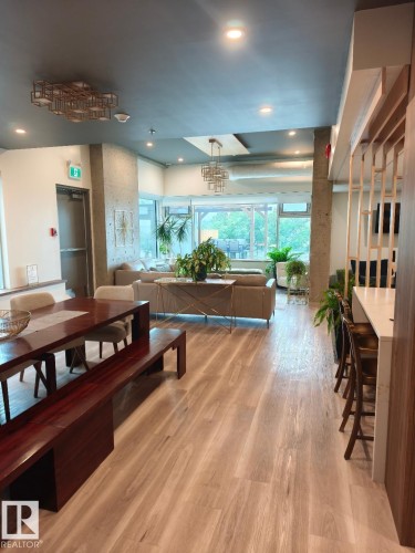 Open-concept area featuring light wood-finish flooring, a dark wood dining table with bench seating, a contemporary chandelier, and large windows providing natural light - 1805 10011 123 Street, Edmonton, AB 