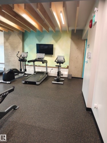 Fitness area featuring wood-slat ceiling accents, integrated linear lighting, a wall-mounted display, and rubberized flooring - 1805 10011 123 Street, Edmonton, AB 