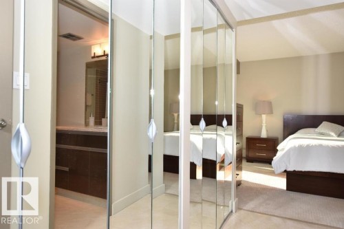 Mirrored closet doors featuring contemporary hardware, with a glimpse of a bathroom vanity and a bedroom - 1805 10011 123 Street, Edmonton, AB 