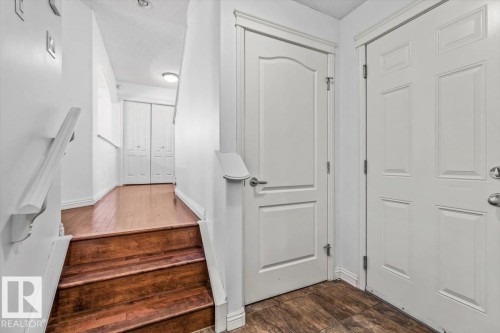 Entryway featuring wood-finish flooring, white paneled doors, and a staircase with wood treads and a white railing - 2407 Hagen Way, Edmonton, AB 