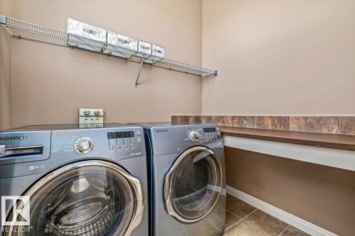 Dedicated laundry area featuring front-loading appliances, a wire storage shelf, and a built-in counter surface with a tiled backsplash - 2407 Hagen Way, Edmonton, AB 