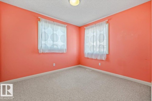 Room featuring two windows with sheer privacy treatments, coral-painted walls, light-colored carpeting, and a ceiling-mounted light fixture - 2407 Hagen Way, Edmonton, AB 