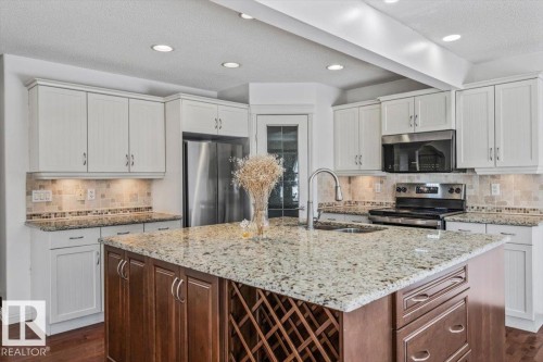 Spacious kitchen featuring an expansive island with a built-in wine rack, light-toned cabinetry, stainless steel appliances, recessed lighting, and wood-finish flooring - 2407 Hagen Way, Edmonton, AB 