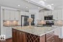 Spacious kitchen featuring an expansive island with a built-in wine rack, light-toned cabinetry, stainless steel appliances, recessed lighting, and wood-finish flooring - 2407 Hagen Way, Edmonton, AB 