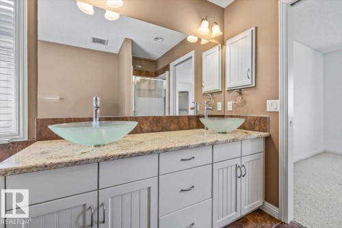 Bathroom vanity featuring dual vessel sinks, a light-toned countertop, and white cabinetry with brushed nickel hardware - 2407 Hagen Way, Edmonton, AB 
