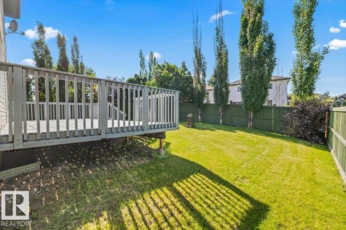 Expansive backyard featuring a wood deck with railings, lush green lawn, mature trees, and privacy fencing - 2407 Hagen Way, Edmonton, AB 