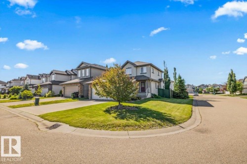 Two-story residence featuring a front attached garage, light-colored siding, and a stone facade accent - 2407 Hagen Way, Edmonton, AB 