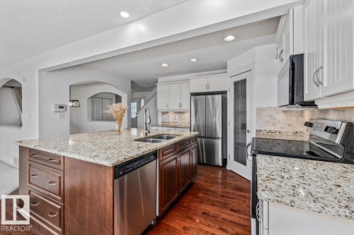Kitchen featuring a large island with a double sink, granite countertops, stainless steel appliances, wood-finish flooring, and recessed lighting - 2407 Hagen Way, Edmonton, AB 