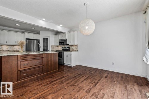 Gourmet kitchen and dining area featuring a two-toned island with ample storage, stainless steel appliances, recessed lighting, and wood-finish flooring - 2407 Hagen Way, Edmonton, AB 