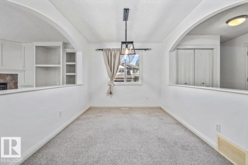 Carpeted room featuring a ceiling-mounted light fixture, a window with a curtain rod, built-in shelving, and white baseboards - 2407 Hagen Way, Edmonton, AB 