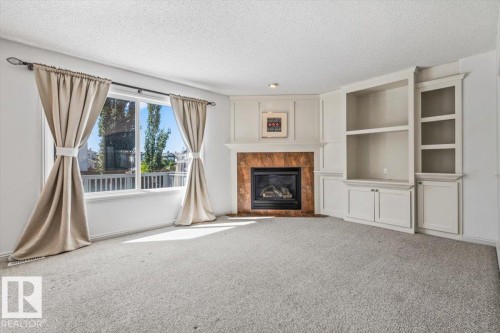 Corner fireplace with a stone surround and a traditional mantel, flanked by built-in cabinetry and shelving - 2407 Hagen Way, Edmonton, AB 