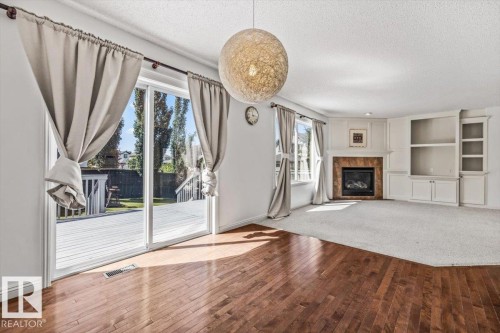 Spacious living area featuring wood-finish flooring transitioning to carpet, a fireplace with a tiled surround, and built-in shelving - 2407 Hagen Way, Edmonton, AB 
