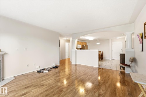 Expansive living space featuring wood-finish flooring - #310 237 Youville Dr E Nw, Edmonton, AB - Indoor Photo Showing Other Room With Fireplace