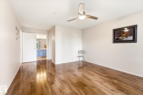 Expansive room featuring wood-finish flooring, a contemporary ceiling fan with integrated lighting, and neutral wall tones - #310 237 Youville Dr E Nw, Edmonton, AB - Indoor Photo Showing Other Room