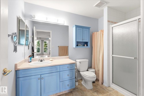 Bathroom featuring a light blue vanity with integrated sink, coordinating wall cabinet, a toilet, and a glass-enclosed shower with tiled walls - #310 237 Youville Dr E Nw, Edmonton, AB - Indoor Photo Showing Bathroom