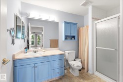 Bathroom featuring a light blue vanity with integrated sink, coordinating wall cabinet, a toilet, and a glass-enclosed shower with tiled walls - 