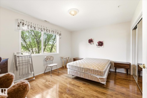 Spacious room featuring wood-finish flooring, a large window, white walls, and a mirrored closet door - #310 237 Youville Dr E Nw, Edmonton, AB - Indoor Photo Showing Bedroom