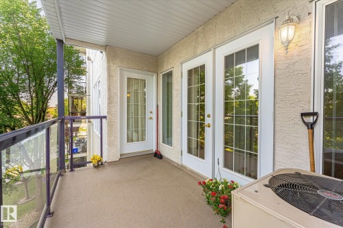 Outdoor balcony with a textured stucco exterior, glass panel railings, and multiple paneled glass doors - #310 237 Youville Dr E Nw, Edmonton, AB - Outdoor With Balcony With Exterior