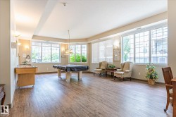 Spacious common room featuring wood-finish flooring, abundant natural light from multiple large windows, and neutral wall tones - 