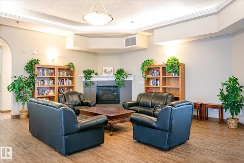 Lounge area featuring a fireplace with tile surround, wood-finish flooring, recessed ceiling with crown molding, and a central chandelier - #310 237 Youville Dr E Nw, Edmonton, AB - Indoor