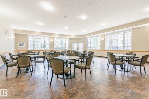 Spacious common area featuring large windows, neutral wall tones, decorative wall sconces, durable tiled flooring, and double-door access - #310 237 Youville Dr E Nw, Edmonton, AB - Indoor Photo Showing Dining Room