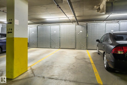 Underground parking garage featuring concrete flooring, overhead lighting, and dedicated storage units with metal grate doors - #310 237 Youville Dr E Nw, Edmonton, AB - Indoor Photo Showing Garage