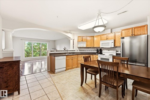 Spacious kitchen featuring wood cabinetry, stainless steel refrigerator, white appliances, and a tiled floor - #310 237 Youville Dr E Nw, Edmonton, AB - Indoor Photo Showing Kitchen With Double Sink