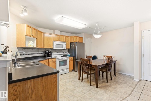 Kitchen featuring wood cabinetry, dark countertops, a tile backsplash, and light-toned flooring - #310 237 Youville Dr E Nw, Edmonton, AB - Indoor Photo Showing Other Room