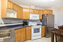 Kitchen featuring wood cabinetry, stainless steel refrigerator, white range, white microwave, and a double basin sink - 