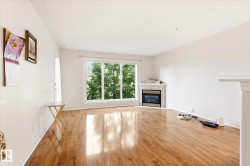 Spacious living area featuring expansive wood-finish flooring, a corner-situated fireplace with a tile surround, and a large bay window offering abundant natural light - 