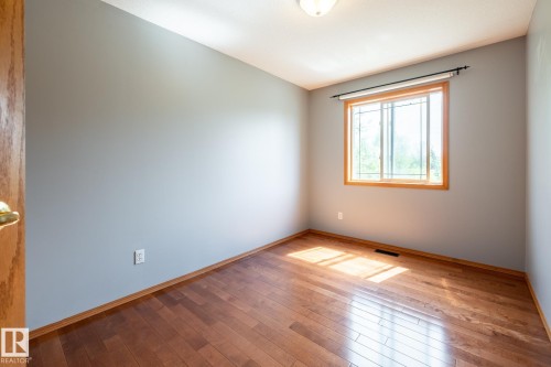 Bedroom featuring wood-finish flooring, a window with wood trim, and light gray walls - 114 Reichert Drive, Beaumont, AB 