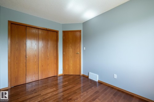 Third bedroom featuring wood-finish flooring, light blue walls, a white ceiling, and wood-panel bifold closet doors - 114 Reichert Drive, Beaumont, AB 