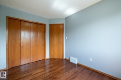 Third bedroom featuring wood-finish flooring, light blue walls, a white ceiling, and wood-panel bifold closet doors - 